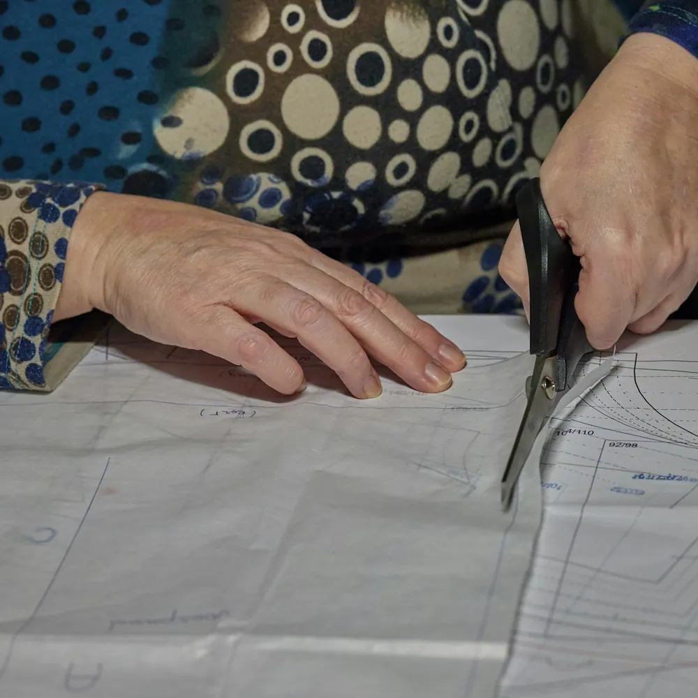 Manos recortando con tijeras un patrón de papel trazado sobre la mesa de un taller de costura